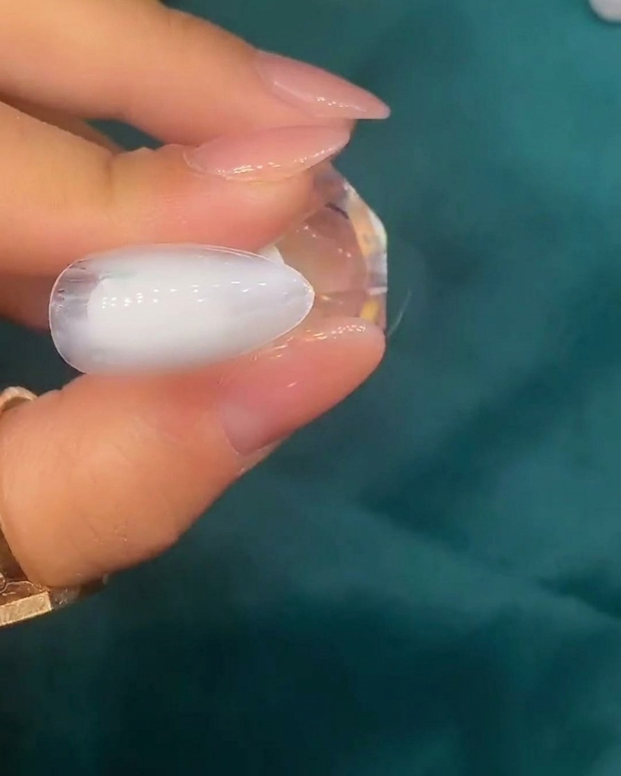 Pinzas colocando pequeñas piezas de concha iridiscente sobre la superficie de una uña con base blanca.