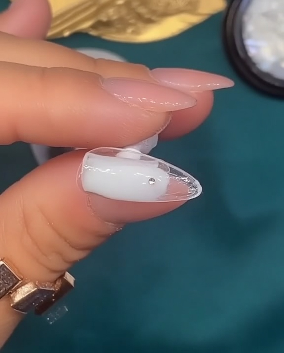 Un pincel aplicando esmalte de gel blanco lechoso sobre una uña con forma natural.