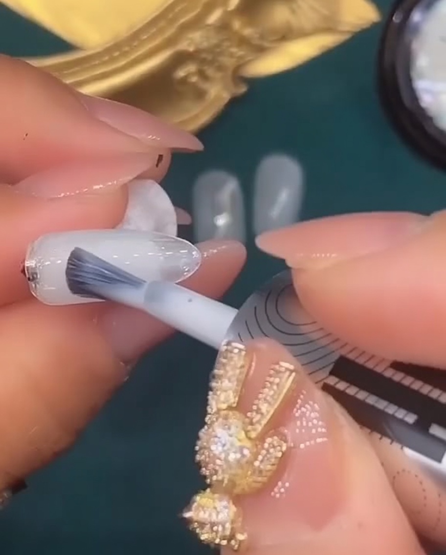 Un pincel aplicando una capa de gel blanco translúcido en la quinta uña.