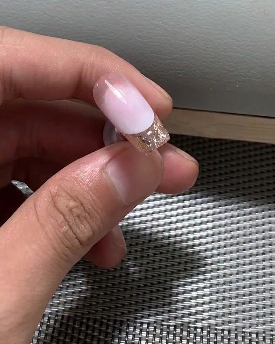 Primer plano de un pincel aplicando una fina capa de esmalte en gel nude sobre la uña.
