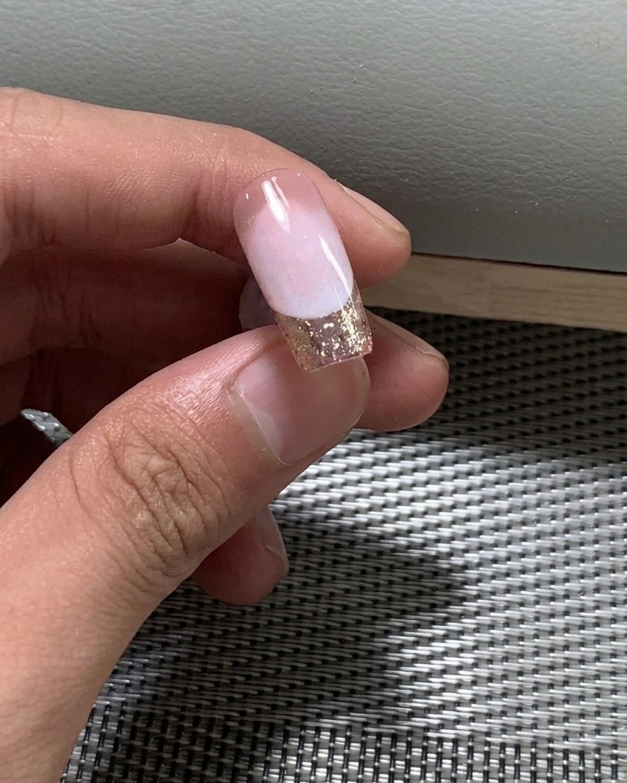 Primer plano de un pincel aplicando una segunda capa de esmalte en gel nude sobre la uña.