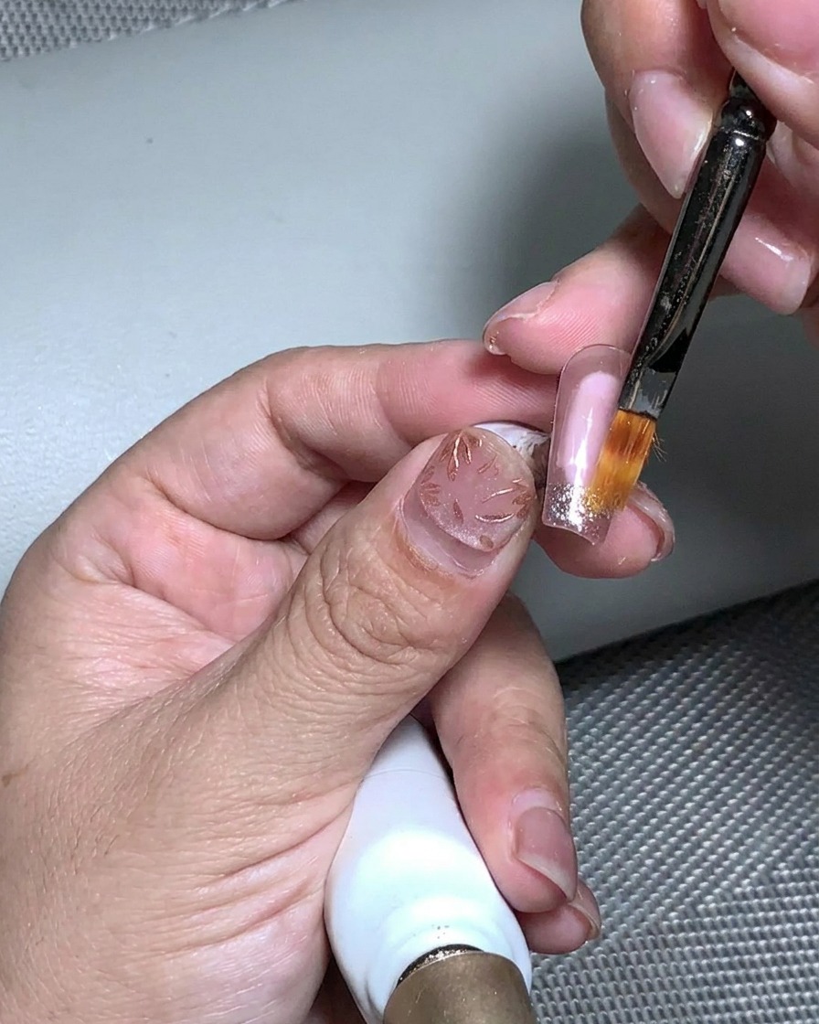 Un pincel aplicando gel de construcción transparente sobre la superficie texturizada con pan de oro y purpurina.