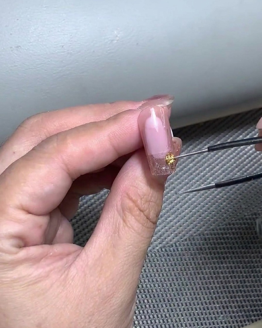 Primer plano de una mano usando pinzas para colocar delicadamente una pegatina curva para francesa sobre una uña preparada.
