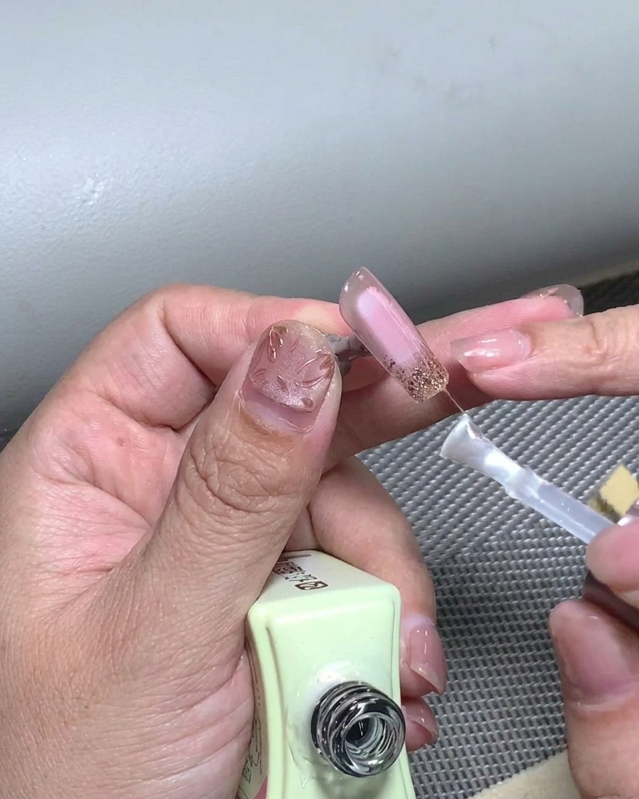 Un pincel aplicando una capa final de top coat transparente sobre un diseño de manicura francesa terminado.