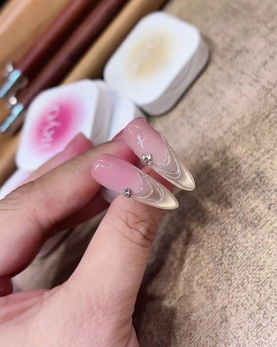 Primer plano de un pincel plano aplicando uniformemente gel nude rosado translúcido sobre una extensión de uña almendrada transparente.