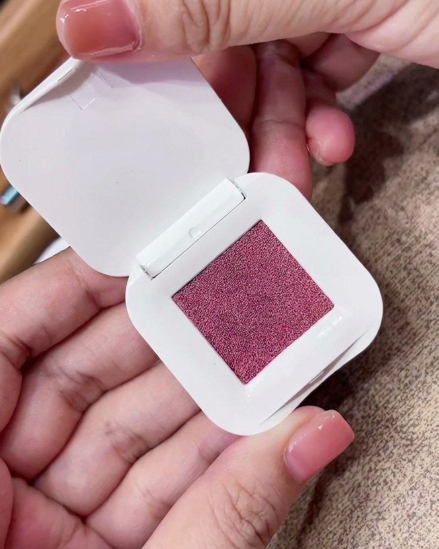 Primer plano de una esponja triangular de maquillaje presionada sobre un compacto de pigmento fino color púrpura rosado.