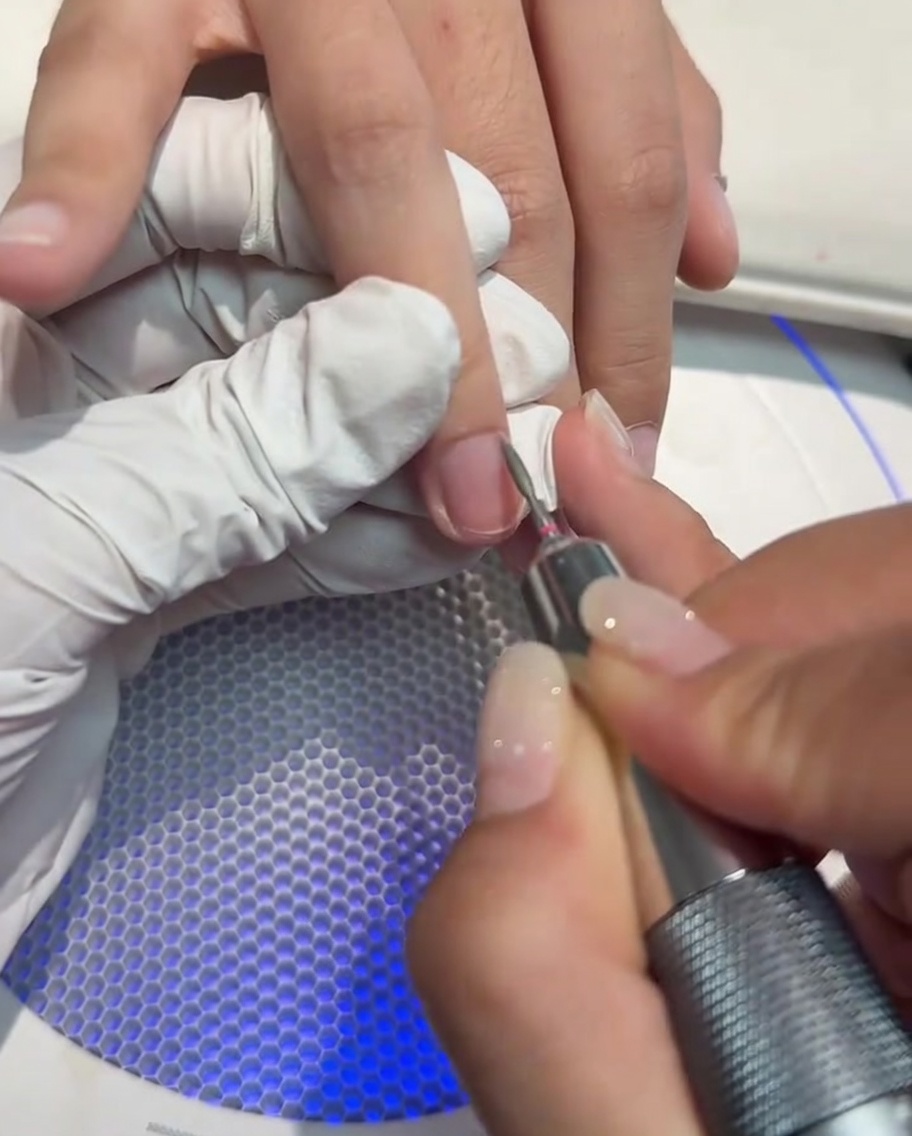 Primer plano de un torno para uñas siendo utilizado para limpiar y abrir el área de la cutícula.