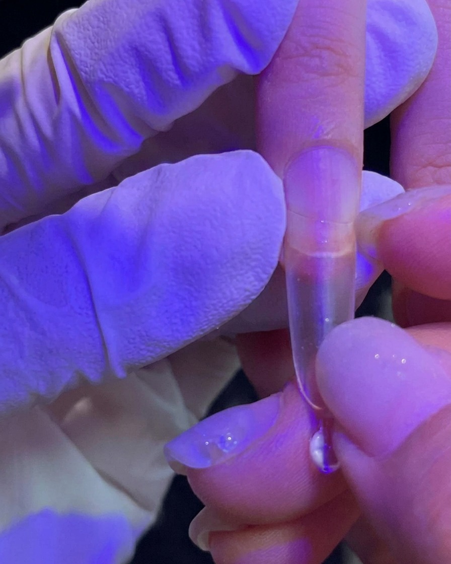 Una mano presionando una punta de extensión transparente sobre una uña natural.