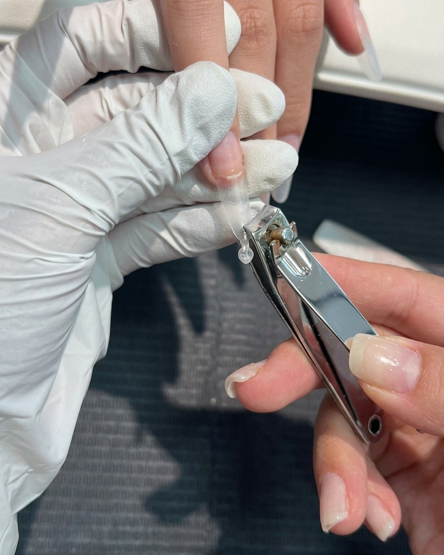 Primer plano de cortaúñas siendo usados para recortar una extensión plástica transparente a la longitud deseada.