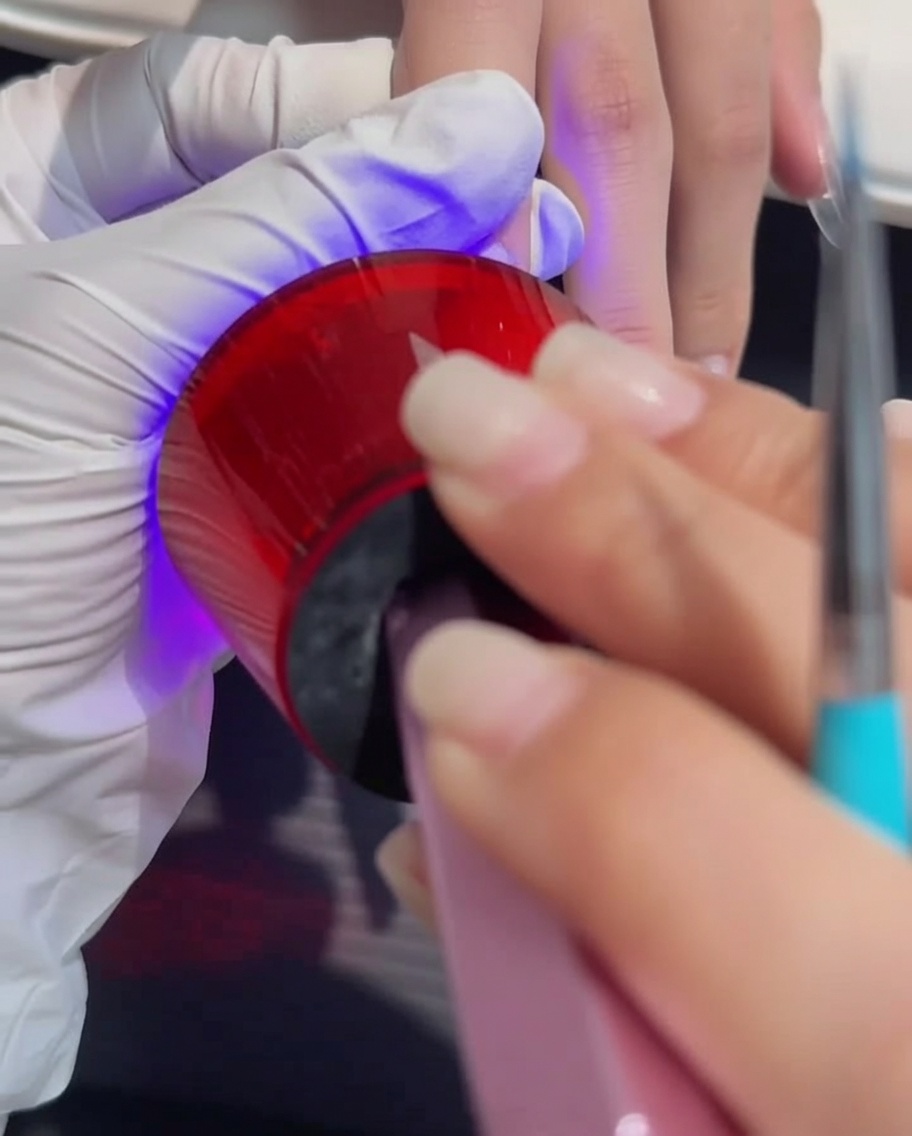 Una mano colocada bajo una lámpara UV/LED profesional durante el proceso de curado del gel.