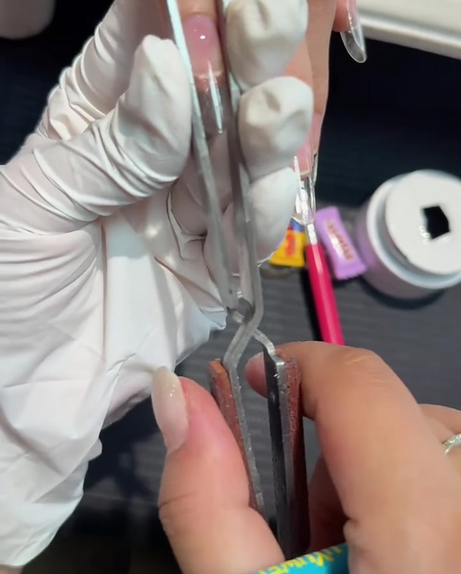 Una herramienta metálica de pinzado siendo usada para estrechar y dar forma a una extensión de gel.