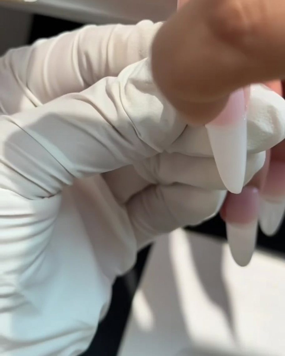Una esponja de maquillaje siendo usada para dar toques de gel blanco lechoso en la punta de una uña para crear un efecto ombré.