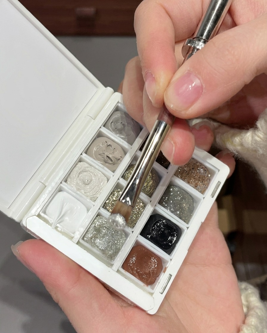 Un pincel mezclando gel de purpurina plateada fina con lentejuelas plateadas más grandes en una paleta blanca de nail art.