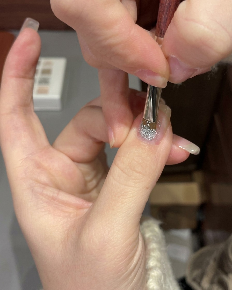 Una mano colocada bajo una lámpara profesional de uñas UV/LED curando una manicura de gel con purpurina.