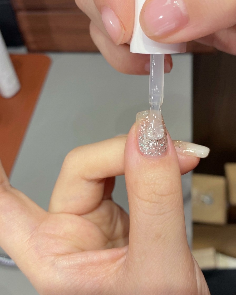 Una mano colocada dentro de una lámpara profesional de uñas UV/LED, con las uñas iluminadas por la luz de curado.