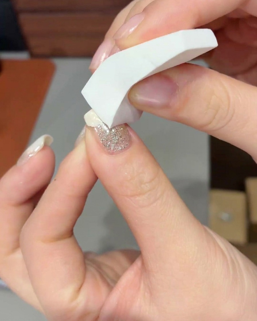 Un primer plano de una esponja de maquillaje aplicando con toquecitos gel blanco lechoso en la punta de una uña para formar un degradado suave.