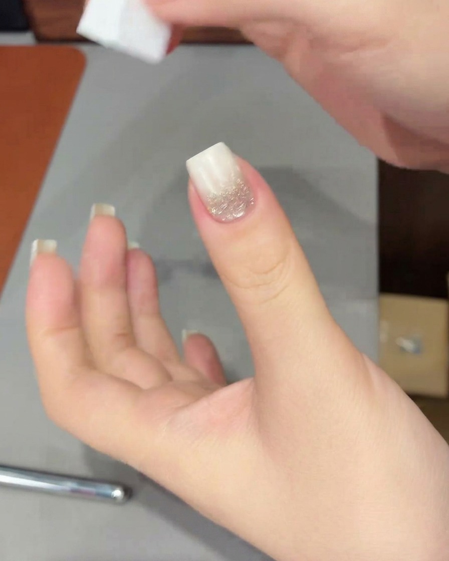 Una mano con una punta degradada blanca colocada dentro de una lámpara UV/LED para curar el gel recién aplicado.
