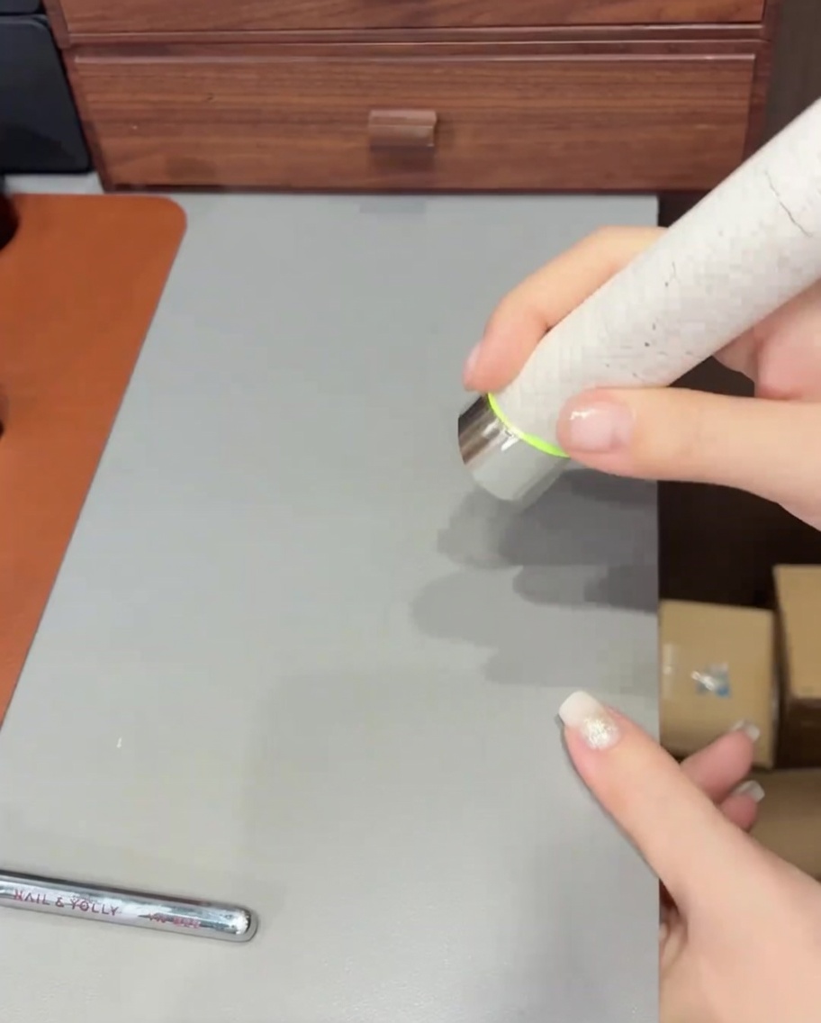 Un pincel aplicando una capa final de top coat transparente sobre una uña con acabado ombré y purpurina.