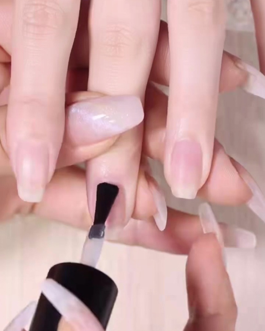 Un pincel de uñas aplicando una capa uniforme de base transparente sobre una uña natural limpia.
