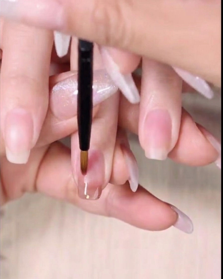 Un pincel fino de detalle barriendo el borde inferior del gel ámbar húmedo hacia abajo para crear un degradado.