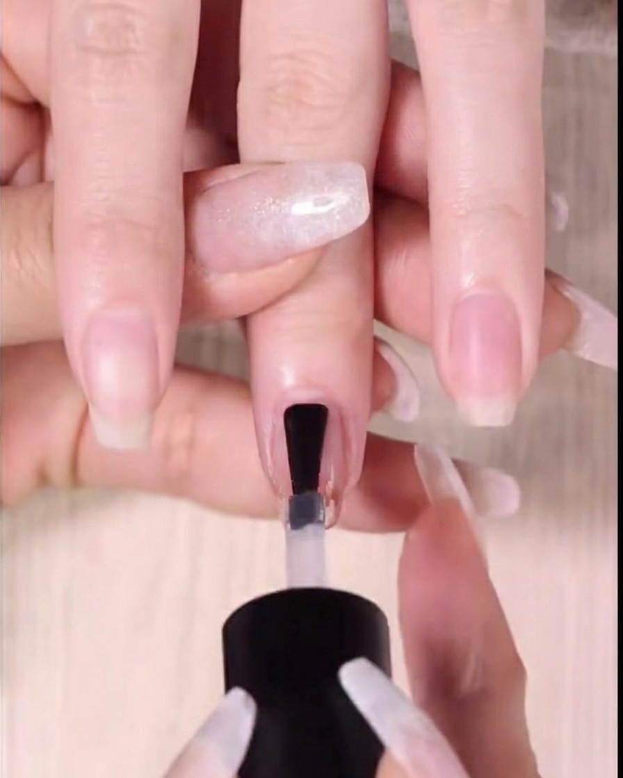 Primer plano de un top coat transparente brillante aplicándose sobre el diseño de uñas degradado ya terminado.