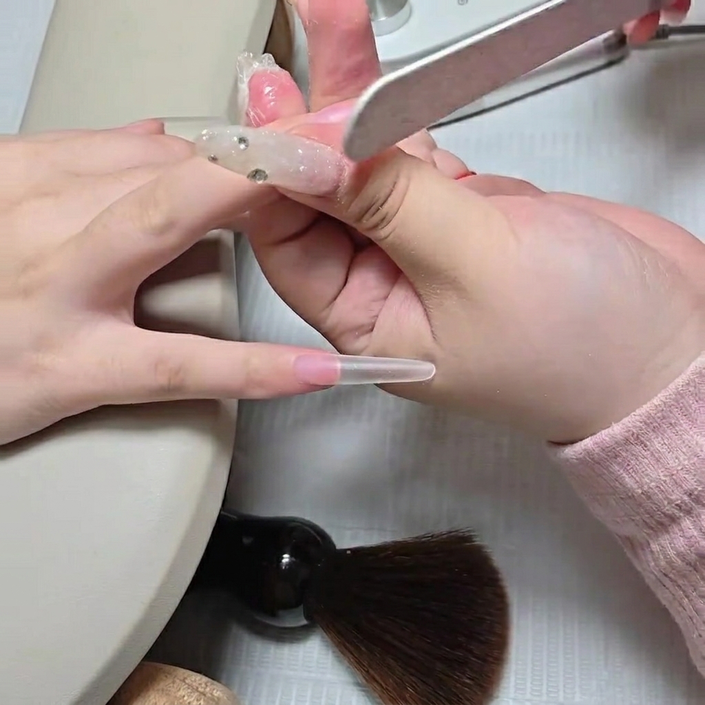 Manicurista usando una lima manual para difuminar la unión donde se encuentra un tip stiletto transparente con la base de la uña natural.