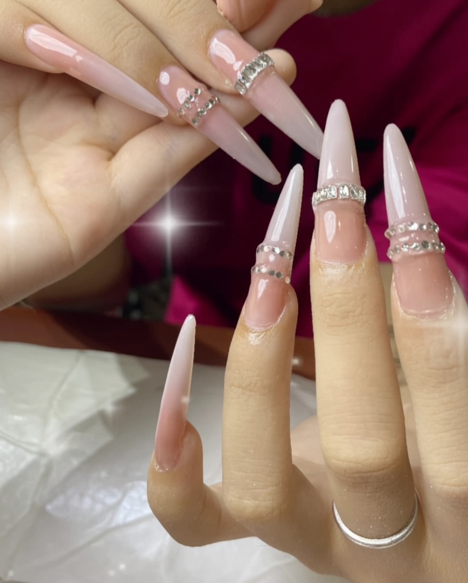 Una mano bajo una lámpara UV, mostrando las uñas con pedrería curándose.