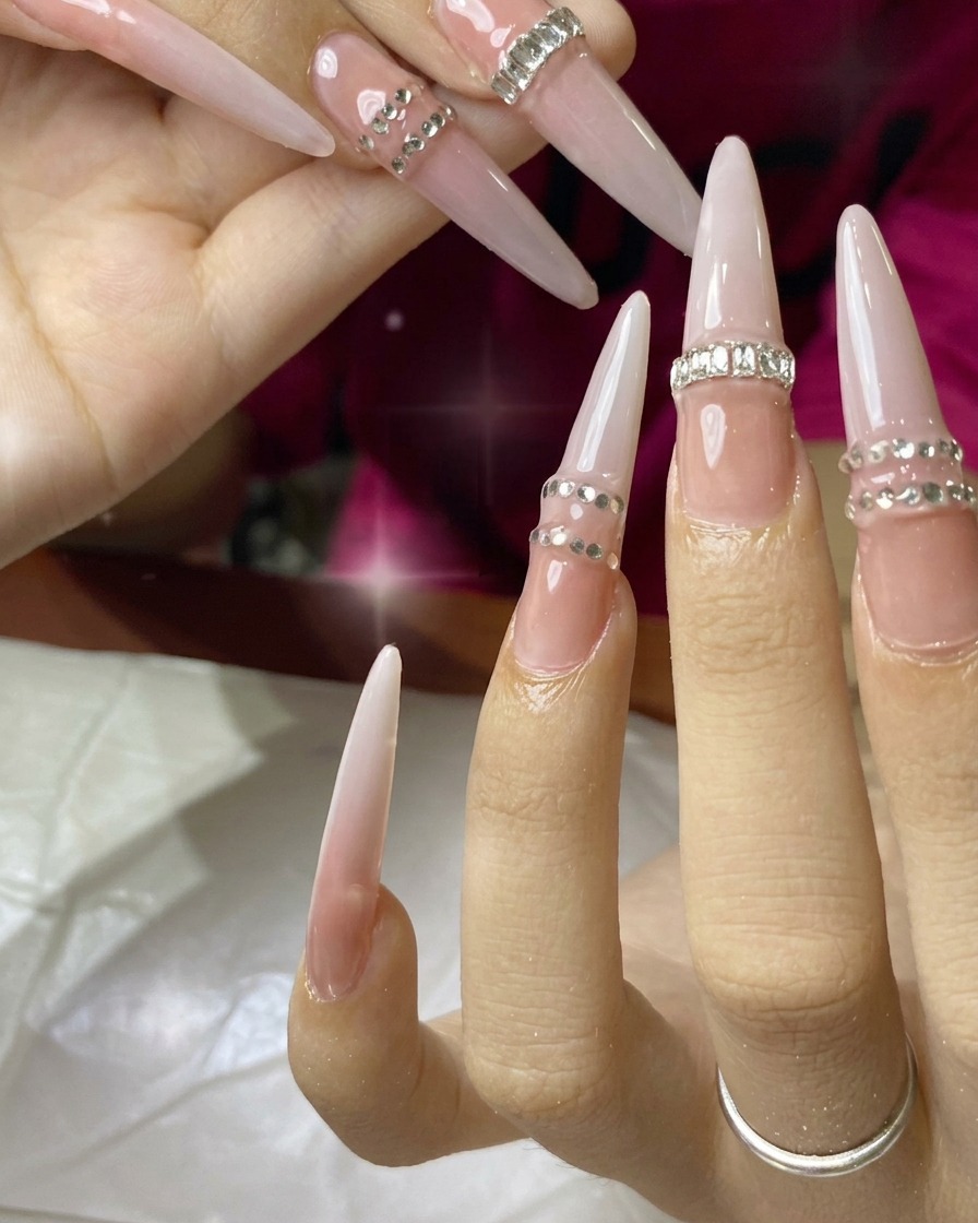 Un pincel de uñas aplicando una capa de esmalte de gel nude sobre una uña de extensión.