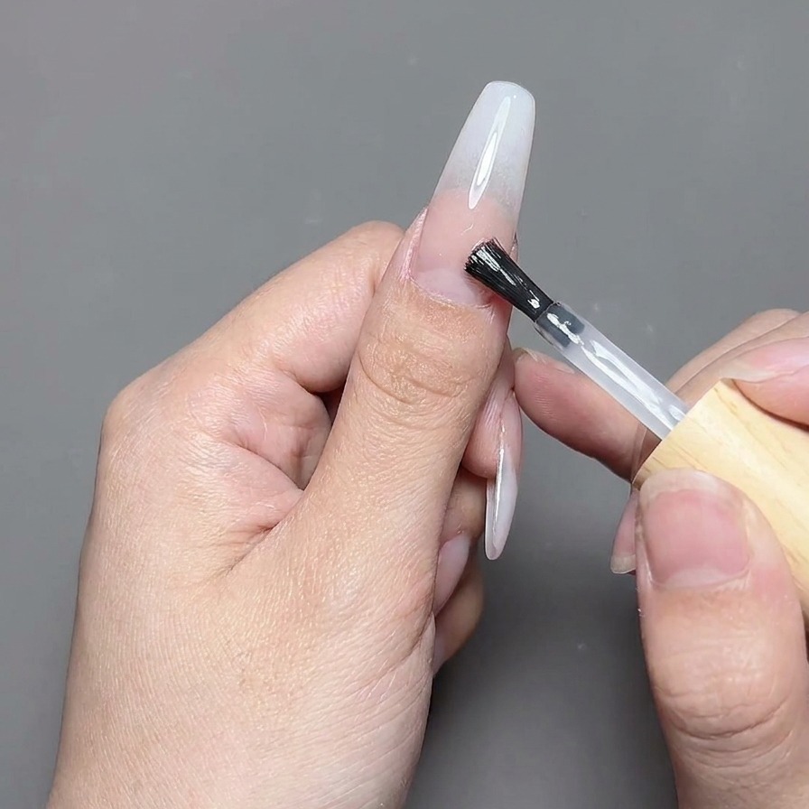 Un pincel aplicando una capa de top coat transparente y brillante sobre un diseño de uñas terminado.