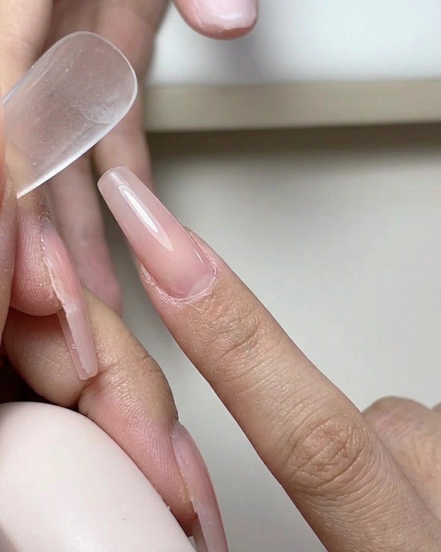 Un pincel aplicando una capa suave y transparente de base de gel sobre la superficie de una uña natural.