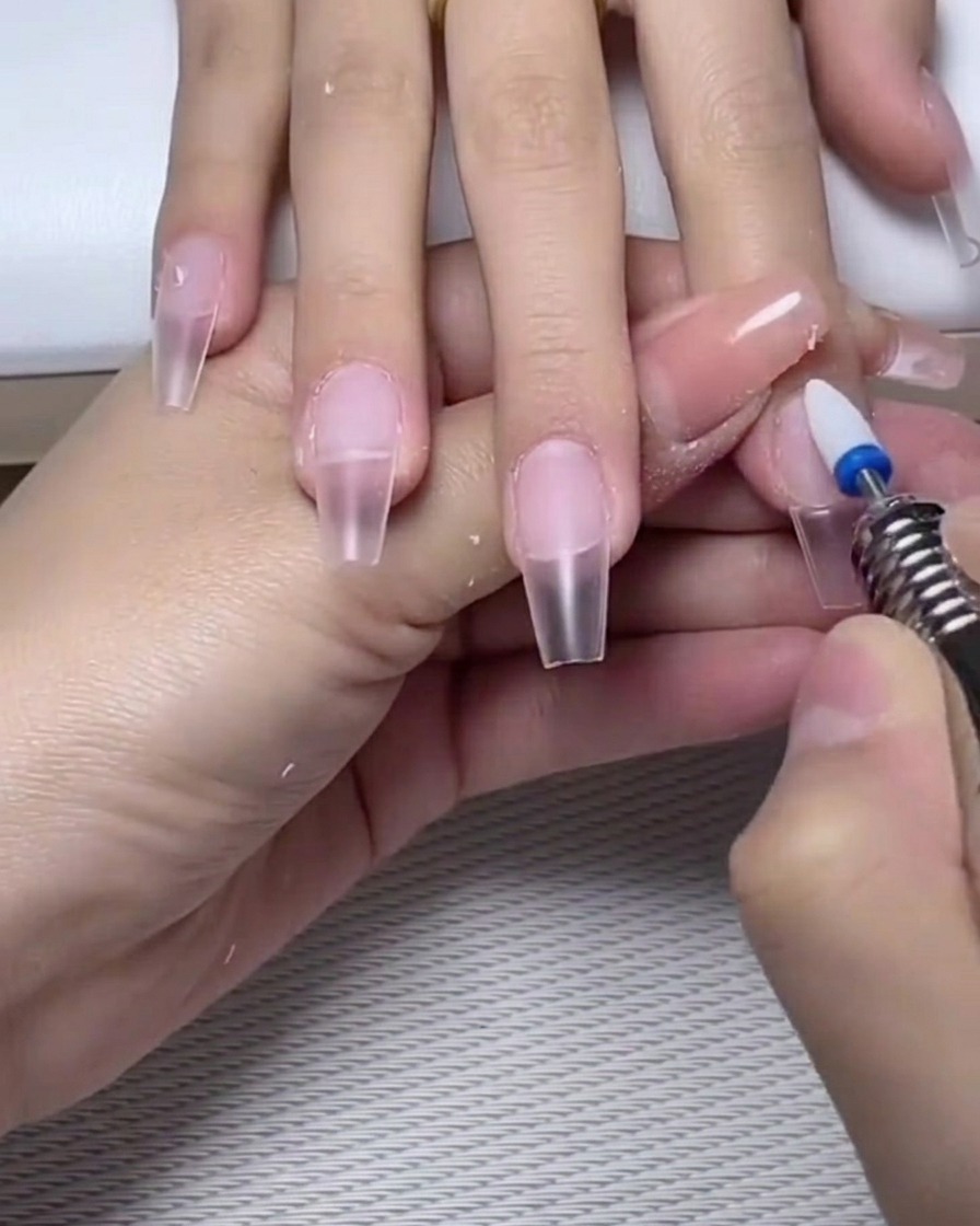 Una lima de uñas puliendo ligeramente la superficie de una base de gel curada sobre la uña.