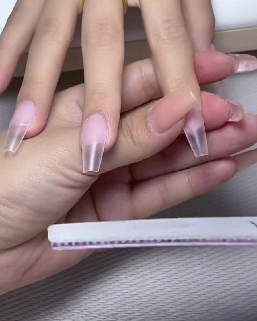 Un pincel de uñas aplicando una capa de esmalte de gel blanco lechoso opaco en la mitad superior de la uña.
