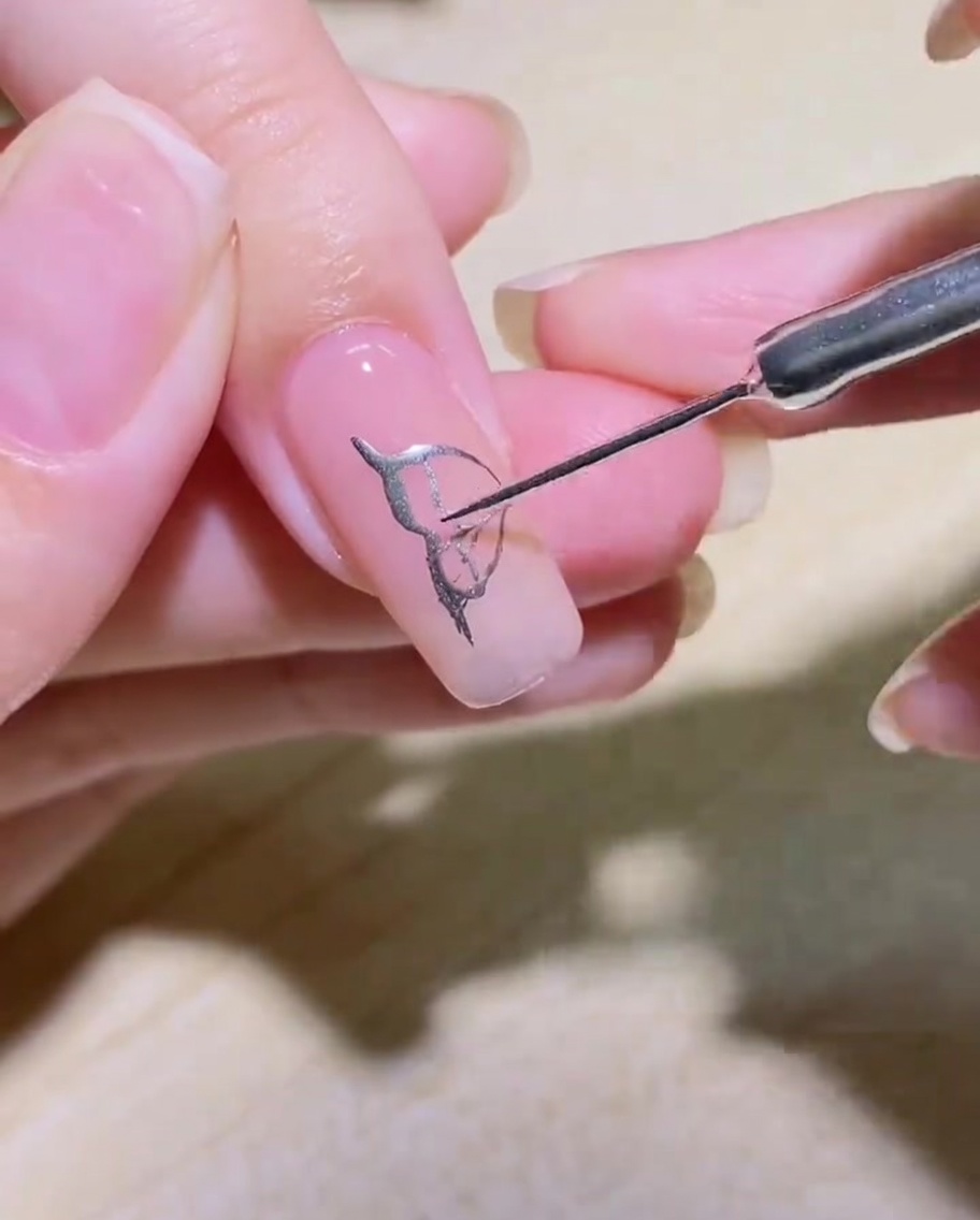 Primer plano de un ala de mariposa rellena de plata con delicados detalles internos sobre una uña.
