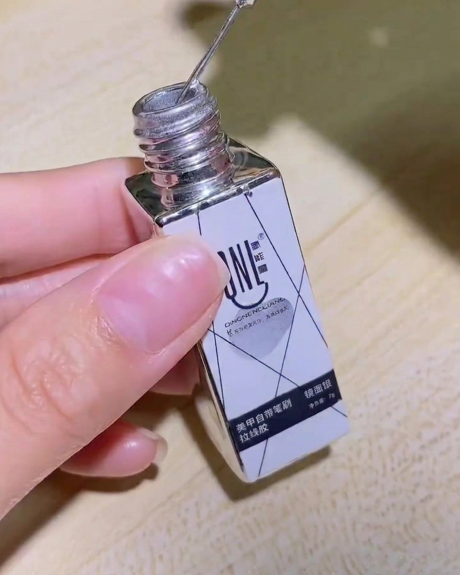 Una mano sosteniendo un frasco de delineador en gel plateado efecto espejo, mostrando la etiqueta claramente.