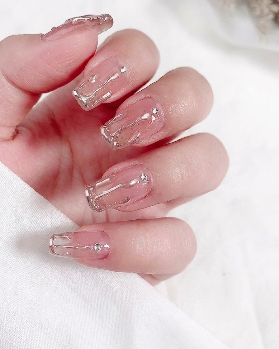 Primer plano de un pincel aplicando una capa de esmalte en gel nude translúcido sobre una uña natural.