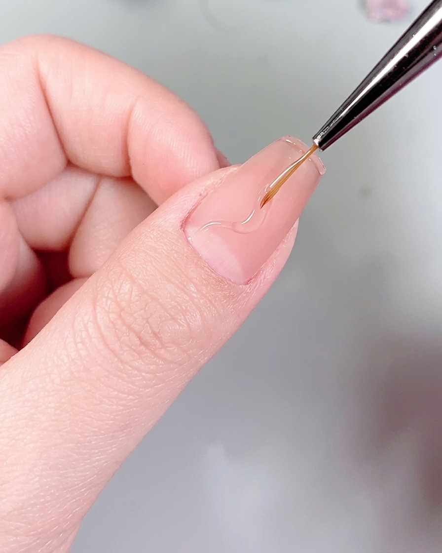 Un pincel liner fino dibujando delicados patrones ondulados de llamas en una uña usando pegamento transparente para uñas.
