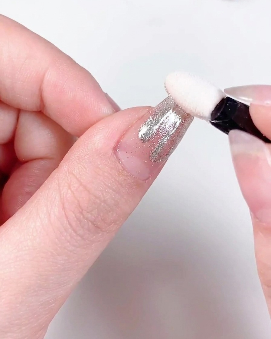 Primer plano de un dedo con patrones de llamas espolvoreados con cromo siendo curado bajo una lámpara profesional de uñas UV/LED.