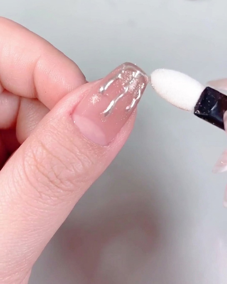 Pinzas sosteniendo un pequeño y brillante cristal y colocándolo en la base de una uña con manicura.