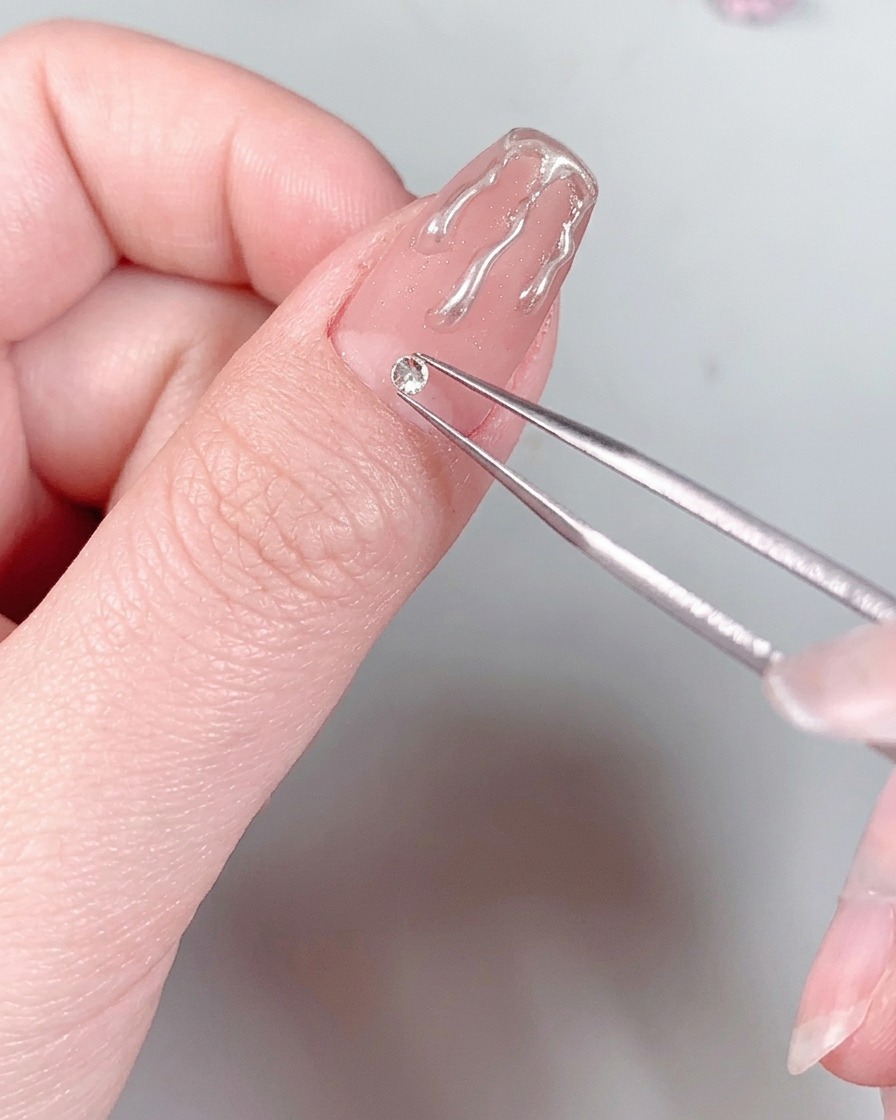 Una uña con manicura y un cristal en la base sostenida bajo la luz de una lámpara UV/LED.