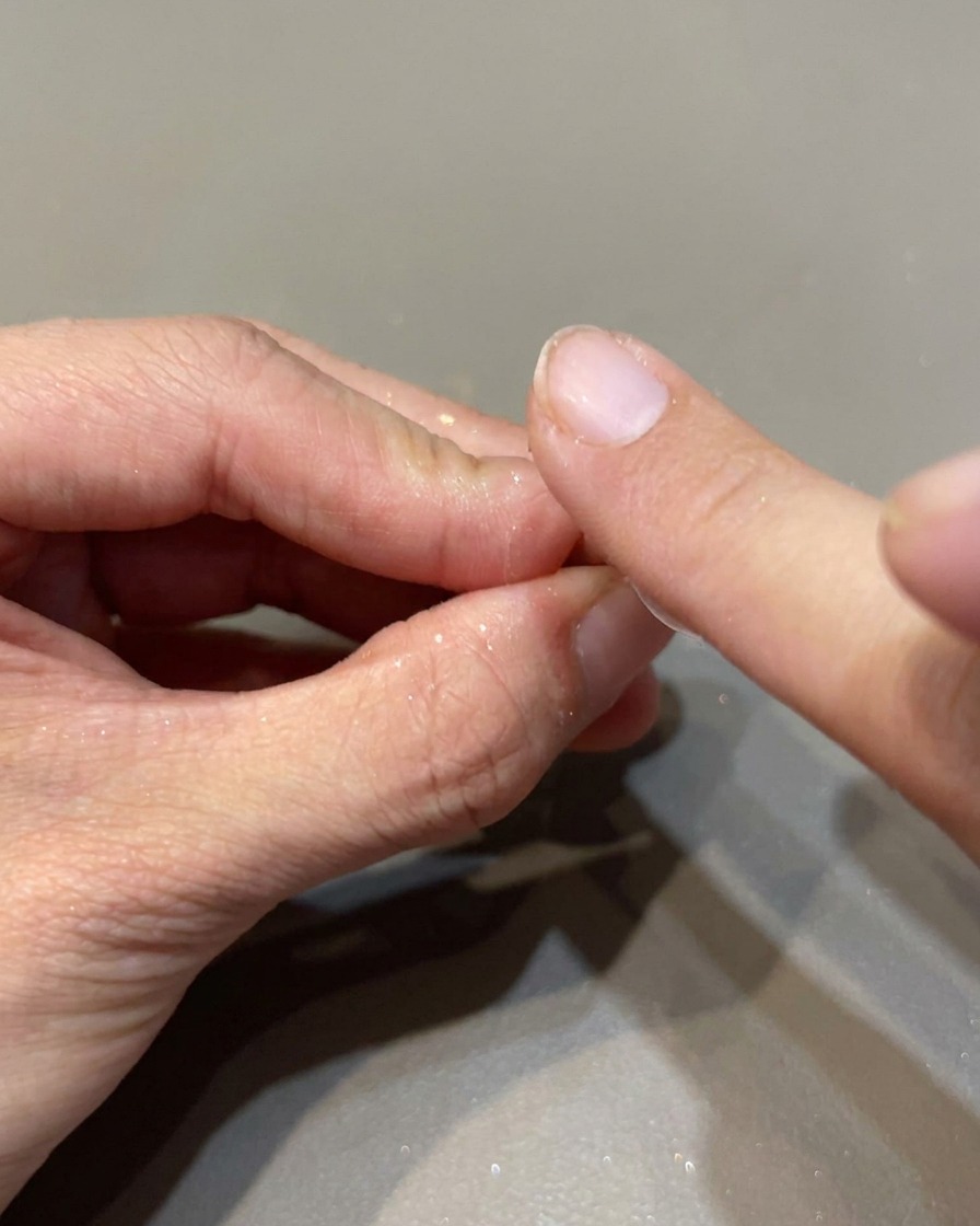 Un aplicador de esponja frotando polvo espejo iridiscente sobre una uña para crear un acabado de alto brillo.