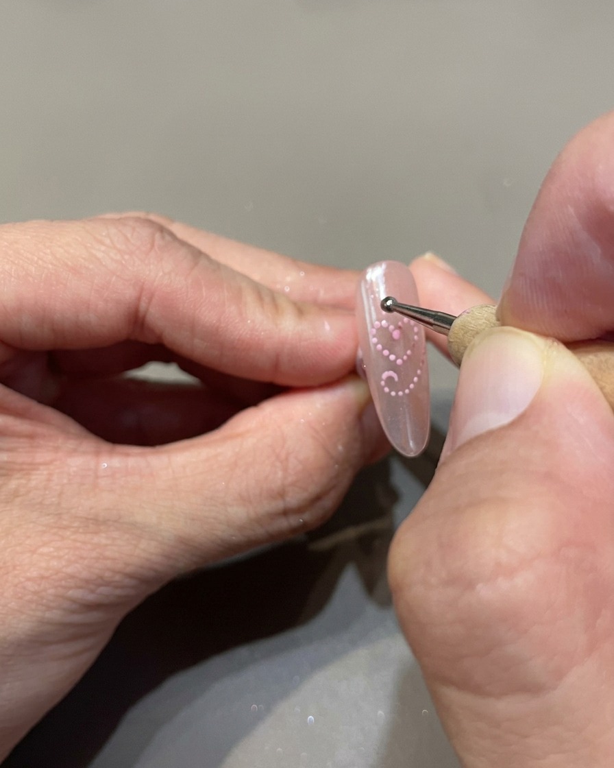 Una herramienta de punteado colocando pequeños puntos uniformes de gel cat-eye rosa para delinear un corazón en la uña.
