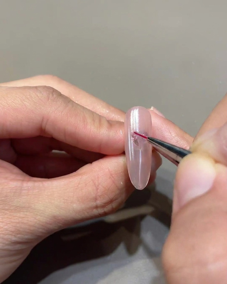 Un pincel delineador de punta fina conectando meticulosamente los puntos de gel para formar un corazón definido y nítido en la uña.