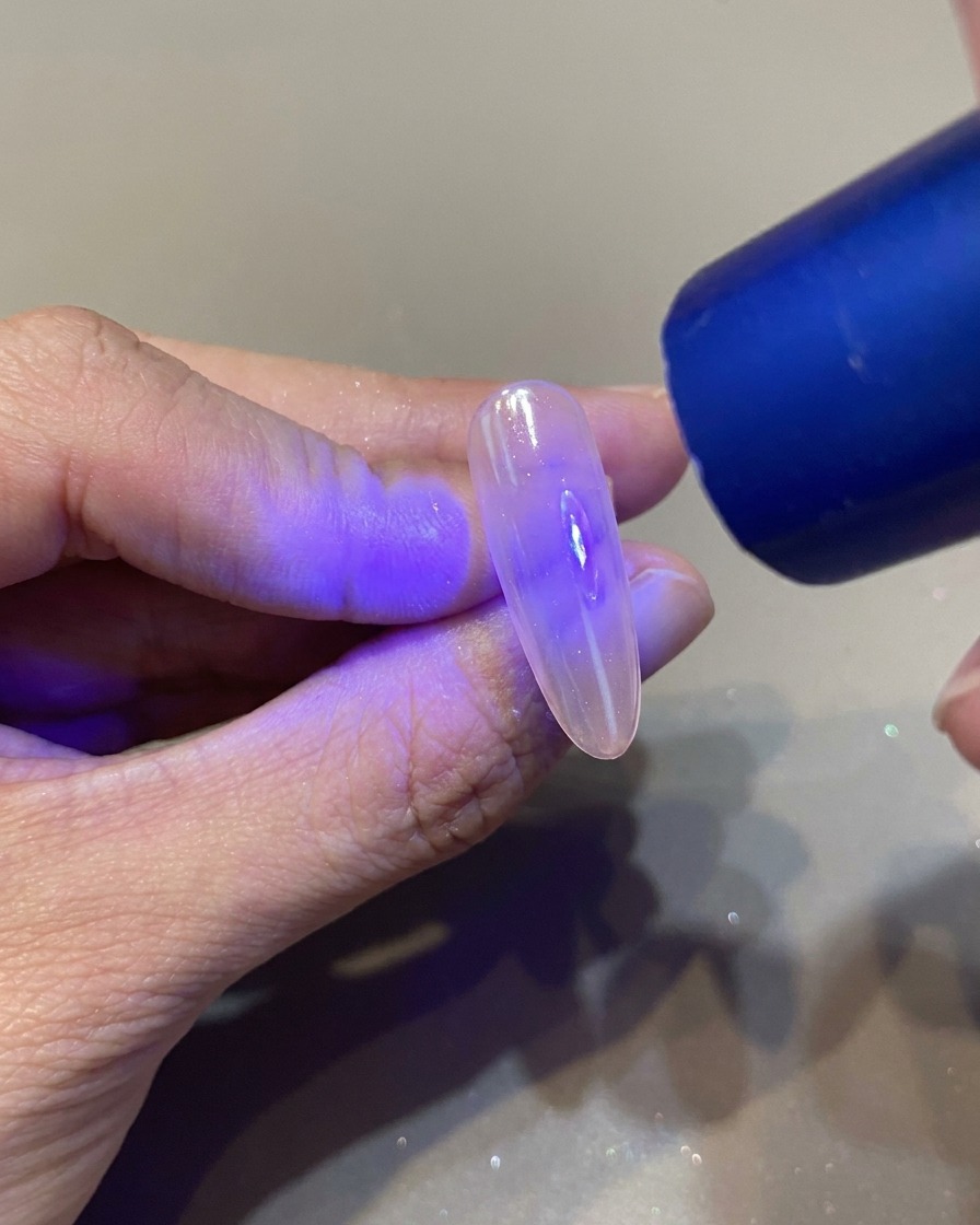 Un pincel de uñas aplicando un top coat transparente y brillante sobre una uña ya decorada.