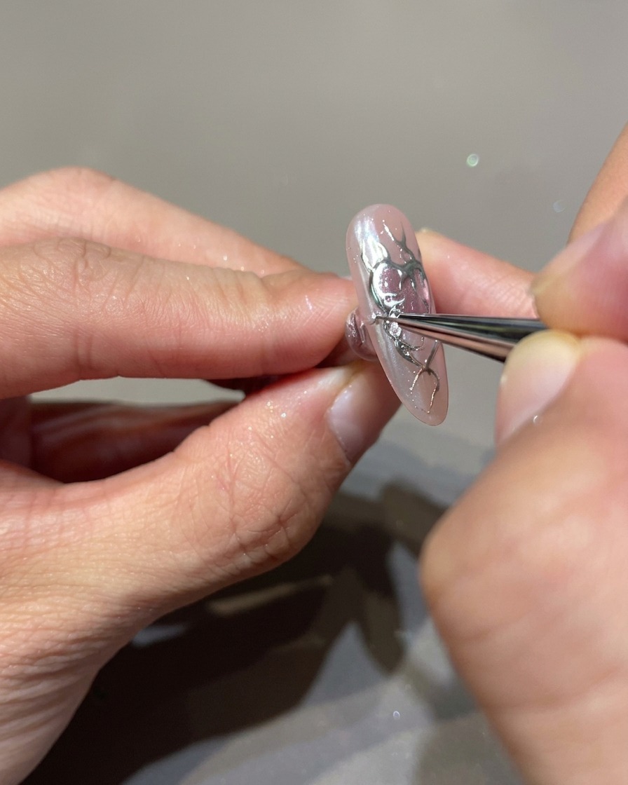 Primer plano de una uña siendo decorada con un pincel fino aplicando gel constructor transparente 3D sobre los contornos de las llamas negras.