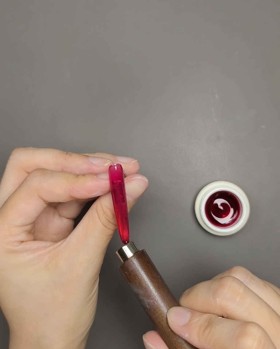Una mano usando un imán de barra cerca de una uña de gel ojo de gato rojo para revelar la línea de brillo magnético.