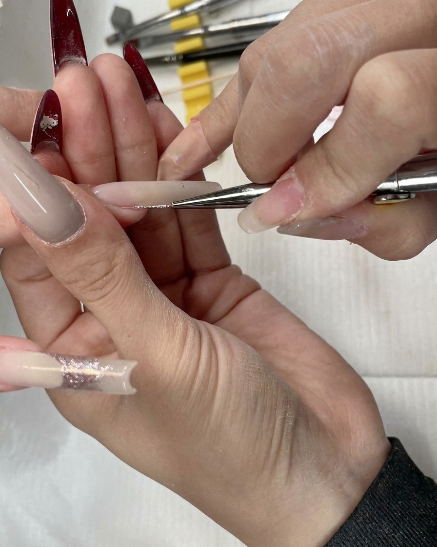 Primer plano de un pincel de detalle aplicando glitter oro rosa sobre la base de la uña.