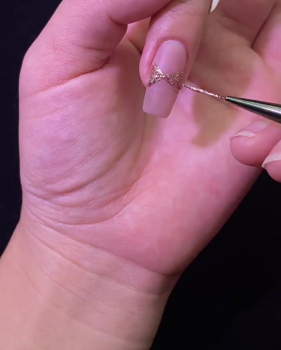 Una uña colocada bajo una lámpara UV/LED para curar el diseño de lazo de glitter.