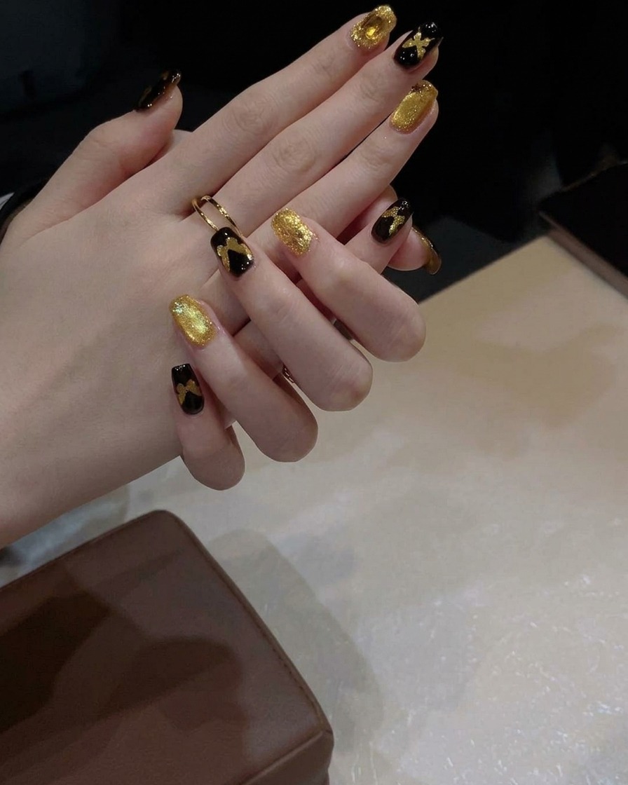 Un pincel de gel aplicando una capa de esmalte cat-eye dorado brillante sobre una uña pintada de negro.