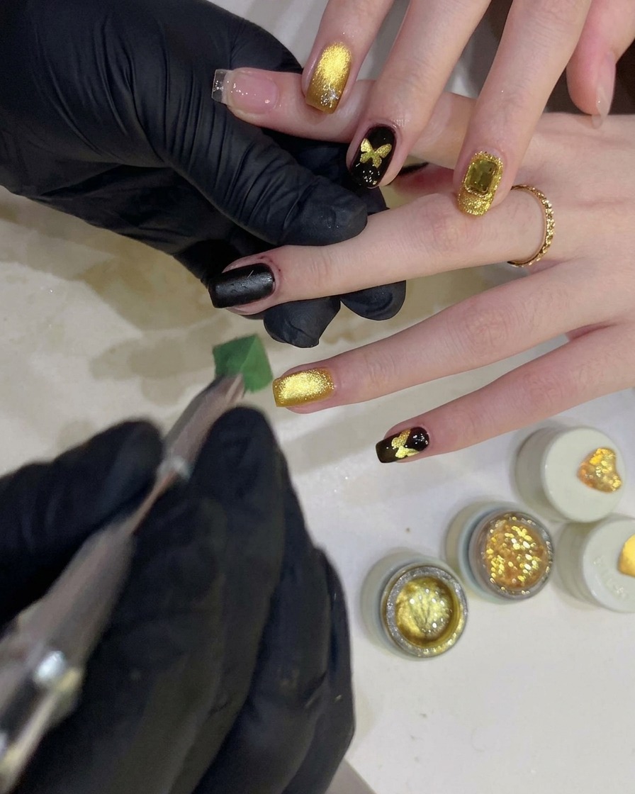Una persona usando una esponja para dar toques de gel negro sobre una plantilla con forma de mariposa en una uña.
