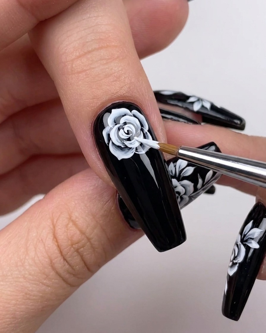 Primer plano de una mano usando un pincel fino para extender líneas de pétalos blancos hacia afuera desde el centro de un diseño floral.